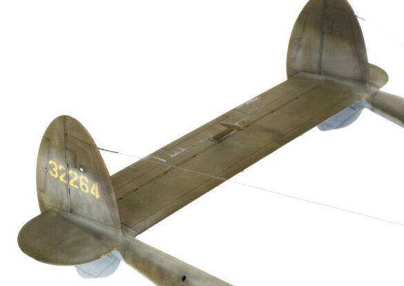 Photo Gallery – Tamiya 1/48 P-38G Lightning by Chris Wauchop Radio compartment detailing using 0.2 mm and 0.3 mm wire – painted placards and realistic wiring. Supercharger units finished with layered metallic and brown/black shades for realistic depth. Fuselage underside showing grime wash and added hydraulic brake lines. Drop tanks weathered for operational realism, mounted underwing. Panel line seal tape simulation using airbrush fading and masking techniques. Camouflage tones stippled for realistic weathered surface finish. Paint wear and black exhaust marks enhance visual realism. Cockpit close-up with foil-made harness and mirror wire control. Wing underside shows soot, staining, and sealing tape simulation. Tail surfaces display extensive weathering and exhaust wear effects.