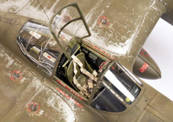 Photo Gallery – Tamiya 1/48 P-38G Lightning by Chris Wauchop Radio compartment detailing using 0.2 mm and 0.3 mm wire – painted placards and realistic wiring. Supercharger units finished with layered metallic and brown/black shades for realistic depth. Fuselage underside showing grime wash and added hydraulic brake lines. Drop tanks weathered for operational realism, mounted underwing. Panel line seal tape simulation using airbrush fading and masking techniques. Camouflage tones stippled for realistic weathered surface finish. Paint wear and black exhaust marks enhance visual realism. Cockpit close-up with foil-made harness and mirror wire control. Wing underside shows soot, staining, and sealing tape simulation. Tail surfaces display extensive weathering and exhaust wear effects.