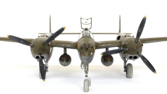 Photo Gallery – Tamiya 1/48 P-38G Lightning by Chris Wauchop Radio compartment detailing using 0.2 mm and 0.3 mm wire – painted placards and realistic wiring. Supercharger units finished with layered metallic and brown/black shades for realistic depth. Fuselage underside showing grime wash and added hydraulic brake lines. Drop tanks weathered for operational realism, mounted underwing. Panel line seal tape simulation using airbrush fading and masking techniques. Camouflage tones stippled for realistic weathered surface finish. Paint wear and black exhaust marks enhance visual realism. Cockpit close-up with foil-made harness and mirror wire control. Wing underside shows soot, staining, and sealing tape simulation. Tail surfaces display extensive weathering and exhaust wear effects.
