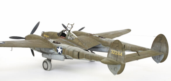Photo Gallery – Tamiya 1/48 P-38G Lightning by Chris Wauchop Radio compartment detailing using 0.2 mm and 0.3 mm wire – painted placards and realistic wiring. Supercharger units finished with layered metallic and brown/black shades for realistic depth. Fuselage underside showing grime wash and added hydraulic brake lines. Drop tanks weathered for operational realism, mounted underwing. Panel line seal tape simulation using airbrush fading and masking techniques. Camouflage tones stippled for realistic weathered surface finish. Paint wear and black exhaust marks enhance visual realism. Cockpit close-up with foil-made harness and mirror wire control. Wing underside shows soot, staining, and sealing tape simulation. Tail surfaces display extensive weathering and exhaust wear effects.