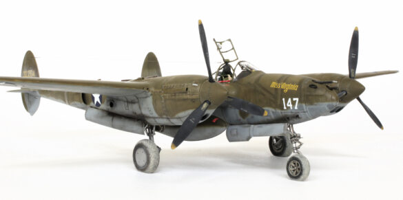 Photo Gallery – Tamiya 1/48 P-38G Lightning by Chris Wauchop Radio compartment detailing using 0.2 mm and 0.3 mm wire – painted placards and realistic wiring. Supercharger units finished with layered metallic and brown/black shades for realistic depth. Fuselage underside showing grime wash and added hydraulic brake lines. Drop tanks weathered for operational realism, mounted underwing. Panel line seal tape simulation using airbrush fading and masking techniques. Camouflage tones stippled for realistic weathered surface finish. Paint wear and black exhaust marks enhance visual realism. Cockpit close-up with foil-made harness and mirror wire control. Wing underside shows soot, staining, and sealing tape simulation. Tail surfaces display extensive weathering and exhaust wear effects.