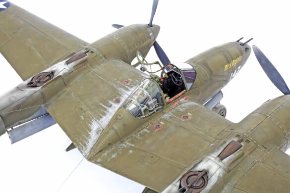 Photo Gallery – Tamiya 1/48 P-38G Lightning by Chris Wauchop Radio compartment detailing using 0.2 mm and 0.3 mm wire – painted placards and realistic wiring. Supercharger units finished with layered metallic and brown/black shades for realistic depth. Fuselage underside showing grime wash and added hydraulic brake lines. Drop tanks weathered for operational realism, mounted underwing. Panel line seal tape simulation using airbrush fading and masking techniques. Camouflage tones stippled for realistic weathered surface finish. Paint wear and black exhaust marks enhance visual realism. Cockpit close-up with foil-made harness and mirror wire control. Wing underside shows soot, staining, and sealing tape simulation. Tail surfaces display extensive weathering and exhaust wear effects.