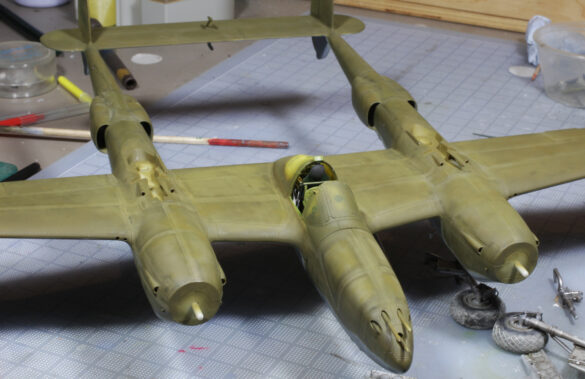 Photo Gallery – Tamiya 1/48 P-38G Lightning by Chris Wauchop Radio compartment detailing using 0.2 mm and 0.3 mm wire – painted placards and realistic wiring. Supercharger units finished with layered metallic and brown/black shades for realistic depth. Fuselage underside showing grime wash and added hydraulic brake lines. Drop tanks weathered for operational realism, mounted underwing. Panel line seal tape simulation using airbrush fading and masking techniques. Camouflage tones stippled for realistic weathered surface finish. Paint wear and black exhaust marks enhance visual realism. Cockpit close-up with foil-made harness and mirror wire control. Wing underside shows soot, staining, and sealing tape simulation. Tail surfaces display extensive weathering and exhaust wear effects.