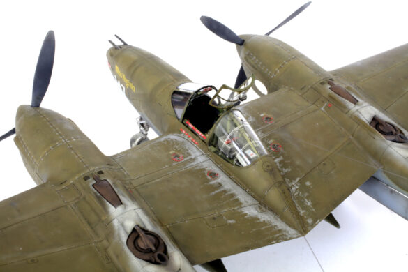 Photo Gallery – Tamiya 1/48 P-38G Lightning by Chris Wauchop Radio compartment detailing using 0.2 mm and 0.3 mm wire – painted placards and realistic wiring. Supercharger units finished with layered metallic and brown/black shades for realistic depth. Fuselage underside showing grime wash and added hydraulic brake lines. Drop tanks weathered for operational realism, mounted underwing. Panel line seal tape simulation using airbrush fading and masking techniques. Camouflage tones stippled for realistic weathered surface finish. Paint wear and black exhaust marks enhance visual realism. Cockpit close-up with foil-made harness and mirror wire control. Wing underside shows soot, staining, and sealing tape simulation. Tail surfaces display extensive weathering and exhaust wear effects.